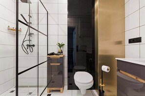 Une salle de bain moderne avec une douche à parois de verre, des toilettes et un meuble-lavabo agrémenté d’une plante.