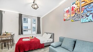 Une chambre à coucher moderne avec un lit, un canapé gris, une table à manger et une fenêtre avec des rideaux.