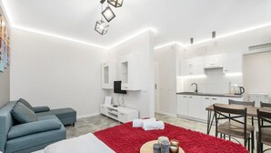 Une pièce moderne et bien éclairée, avec un canapé, un tapis rouge et un coin repas comprenant des chaises et une table.