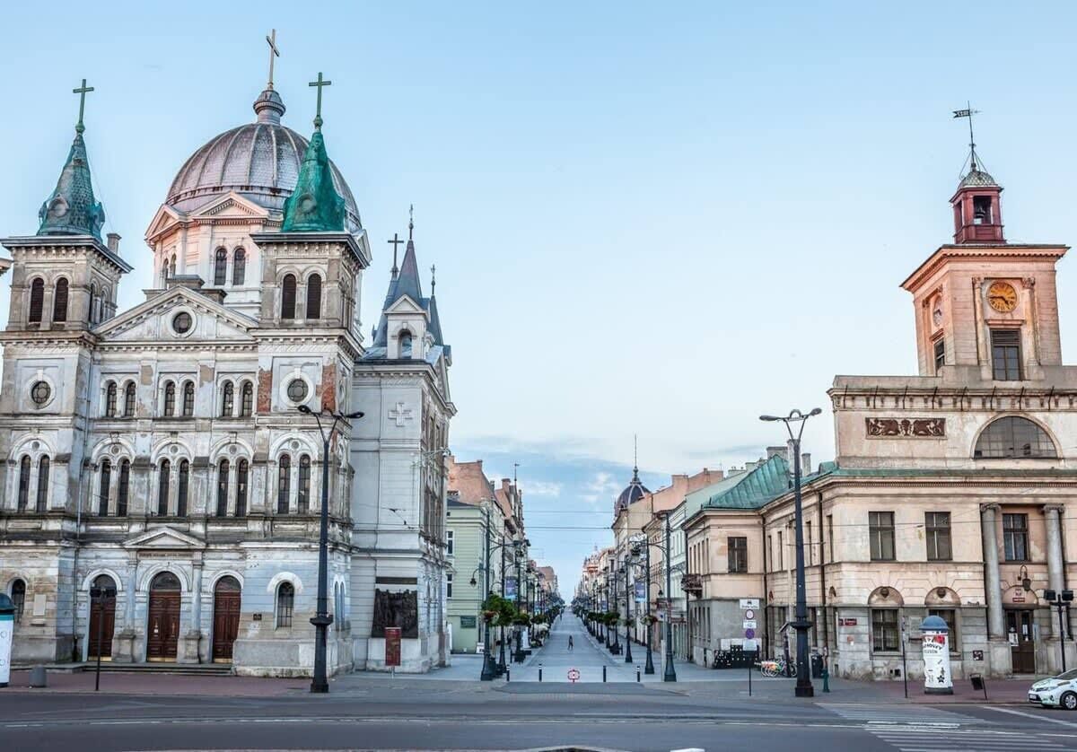 Vista de una calle con edificios históricos, incluyendo una iglesia con cúpula y cruces, y una torre del reloj.
