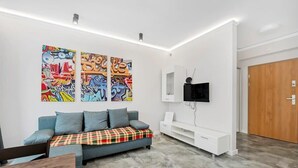 Un salon moderne avec un canapé gris, un plaid et des œuvres de graffiti colorées sur le mur.