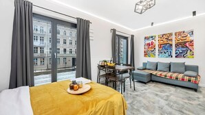 Une chambre d’hôtel moderne comprenant un lit, une table à manger avec des chaises, un canapé et une grande fenêtre avec des rideaux.