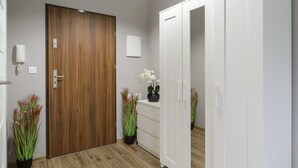 A hallway with a wooden door, white wardrobe, and potted plants. - Lumina modern studio with balcony (Łódź)