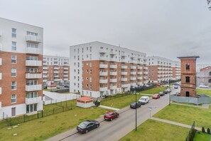 A multi-story residential building with balconies, a parking area, and a small brick tower. - Lumina modern studio with balcony (Łódź)