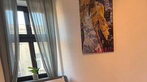 Ein Schlafzimmer mit Bett, einem Fenster mit Vorhängen, einem Topf mit Pflanze und einer Wand mit einem farbenfrohen Poster.