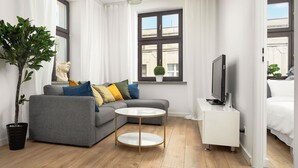 Ein modernes Wohnzimmer mit einem grauen Sofa, einem runden Couchtisch, einem Fernseher auf einem weißen Schrank und einer topfpflanzten Pflanze.