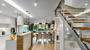 Eine moderne Küche mit einer zentralen Kochinsel, ein Essbereich mit Blick und eine Treppe mit Holzvertäfelung.