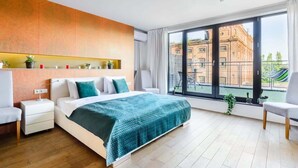 Ein modernes Hotelzimmer mit einem großen Bett, einem Nachttisch, einem Sessel, einem Balkon mit Blick auf ein Gebäude und einem Regal mit Dekoration.