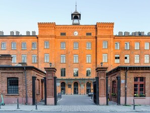 Un grand bâtiment en briques, doté d’un beffroi central, de nombreuses fenêtres et d’une façade symétrique.