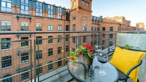 Ein Balkon mit rundem Tisch, einem Blumentopf und einem Glas Wein.