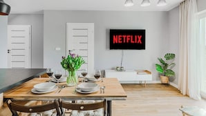 Un comedor moderno con una mesa de madera dispuesta para cuatro comensales, un televisor en la pared y una planta en maceta.