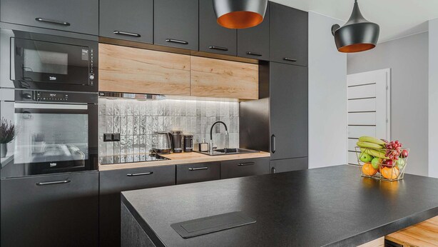 Una cocina moderna con armarios oscuros, encimera de madera, horno empotrado, fregadero e iluminación colgante.