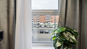 Vista desde una ventana con cortinas, un estacionamiento y un edificio con varios pisos y balcones.