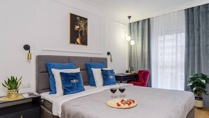 Un dormitorio moderno con una cama grande, una mesita de noche con lámpara, un escritorio con silla y una ventana con cortinas.