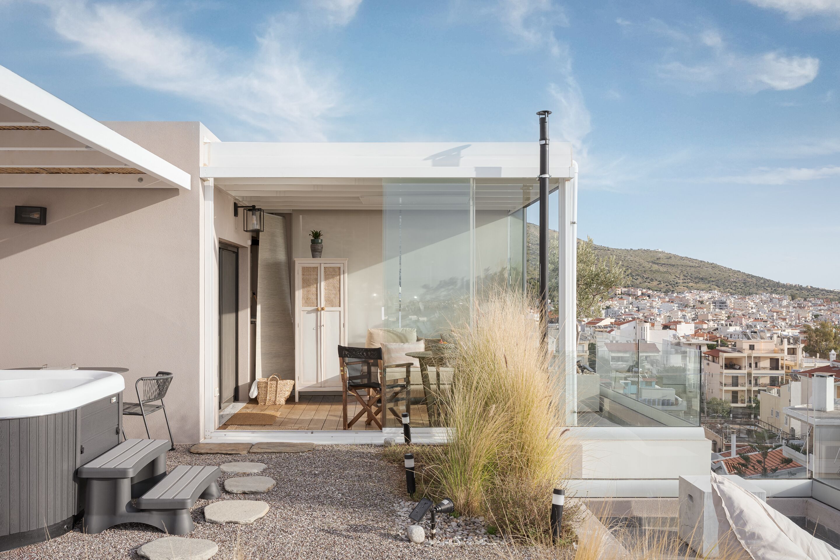 Una terraza moderna en la azotea con jacuzzi, zona de estar y barandilla de cristal con vistas a la ciudad.