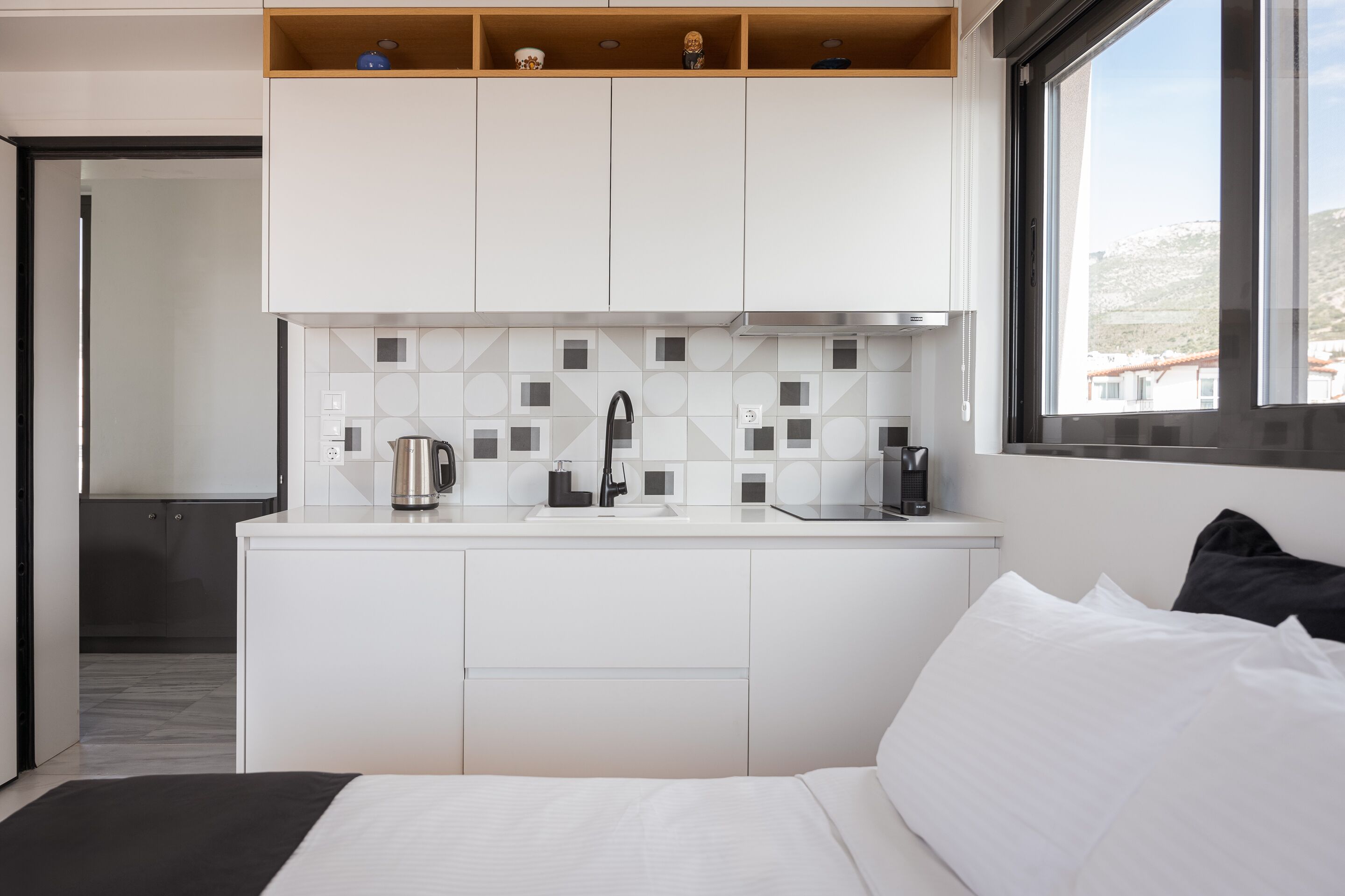 Una camera d'albergo moderna con un letto, un angolo cottura con macchina del caffè e una finestra vista edifici.