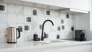 Una cocina moderna con armarios blancos, un hervidor de acero inoxidable, una cafetera negra y un salpicadero con diseño geométrico.