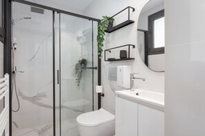 A modern bathroom with a glass-enclosed shower, a white toilet, a sink, and a mirror. - Glyfada Panoramic Penthouse (Glyfada)
