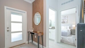 Corredor que dá para um quarto, com uma toucador, espelho e porta com painéis de vidro jateado.