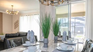 Uma sala de jantar com uma mesa de mármore, cadeiras de couro preto e um lustre moderno.