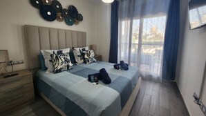 Un dormitorio con cama, mesitas de noche, lámpara, reloj de pared y ventana con cortinas.