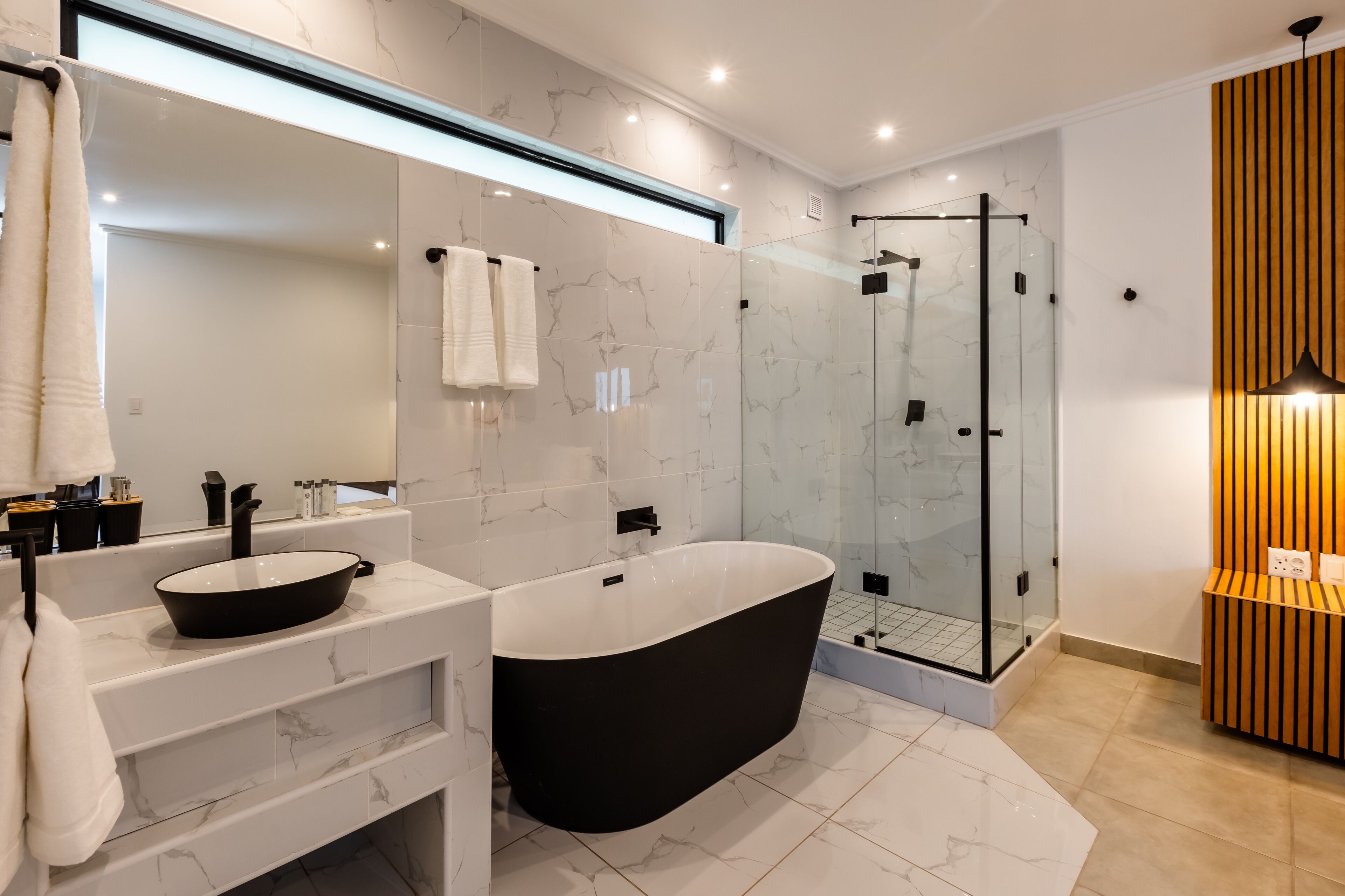Un baño moderno con una bañera independiente, ducha con mampara de vidrio y tocador con lavamanos y espejo.
