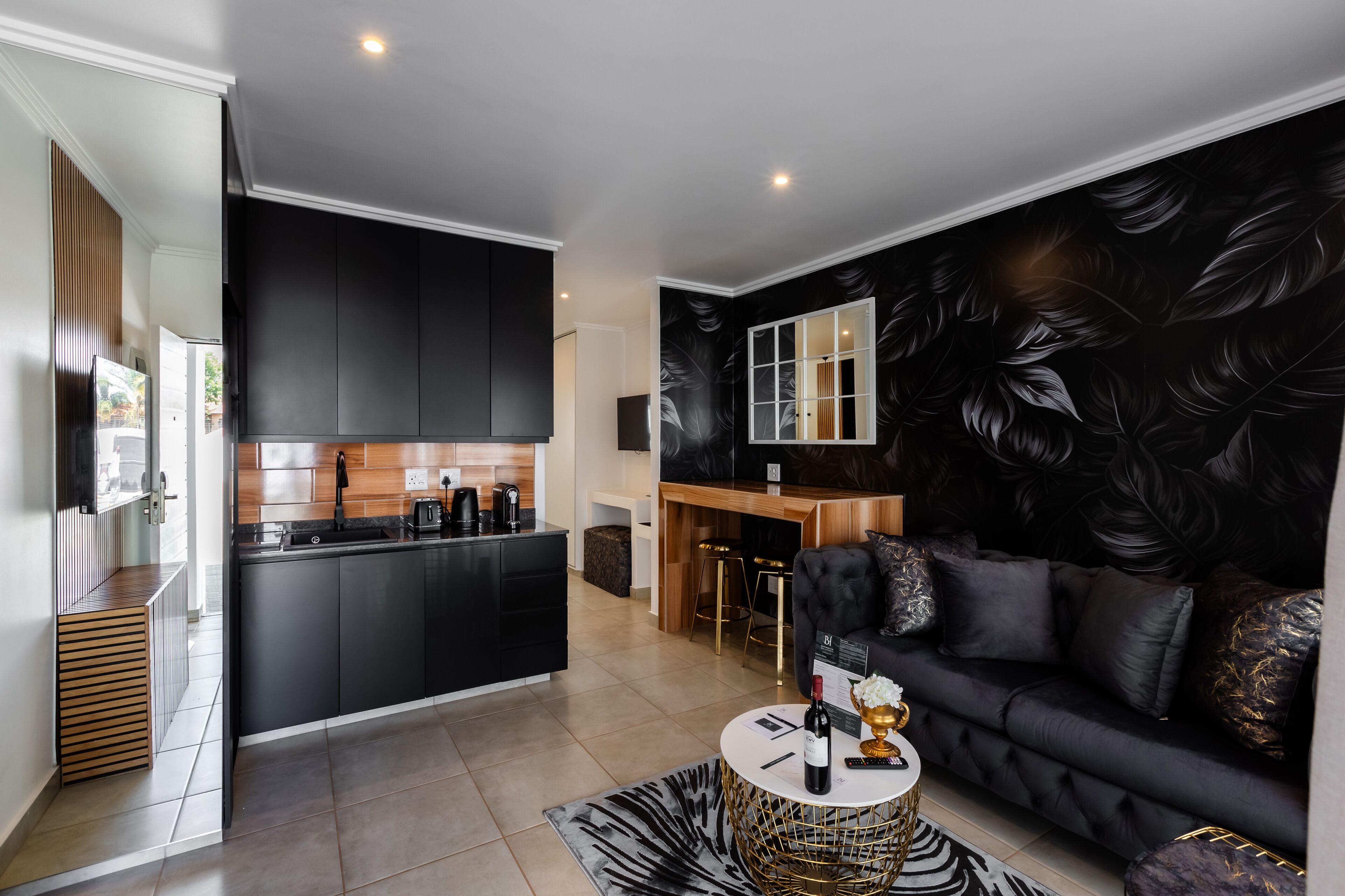 A modern living space with a kitchen, dining area, and a black leather sofa.