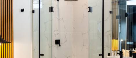 A modern bathroom with a glass-enclosed shower, marble tiles, a wooden bench, and a large mirror.