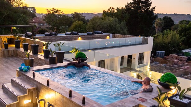 Una piscina infinita en la azotea con barandilla de vidrio, rodeada de plantas en macetas y velas.