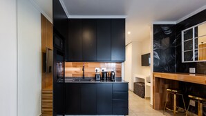 Una cocina moderna con armarios negros, encimera de madera y dos taburetes dorados.