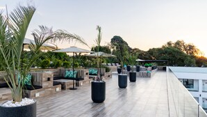 Una terraza en la azotea con zonas de estar, jardineras y sombrillas.
