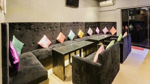 A row of black cushioned booths with colorful pillows, a glass partition, and a tiled floor.