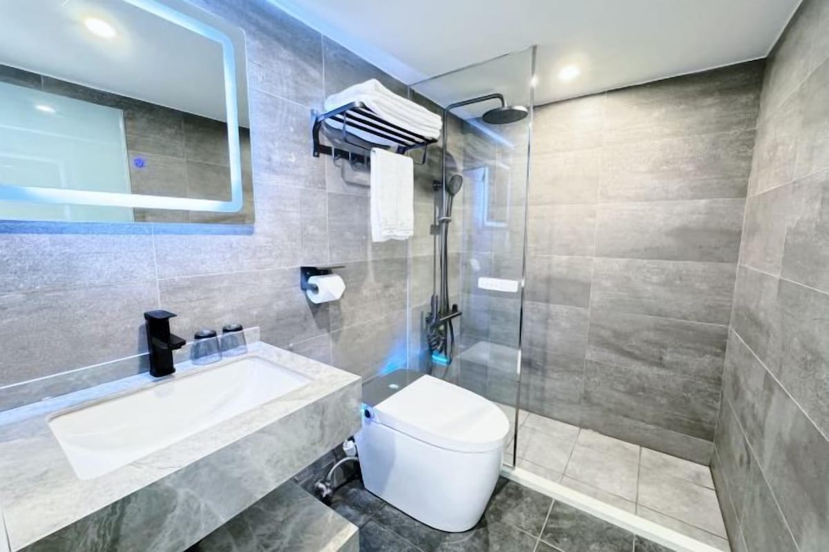 Un baño moderno con ducha de vidrio, inodoro blanco y un amplio lavabo de mármol.
