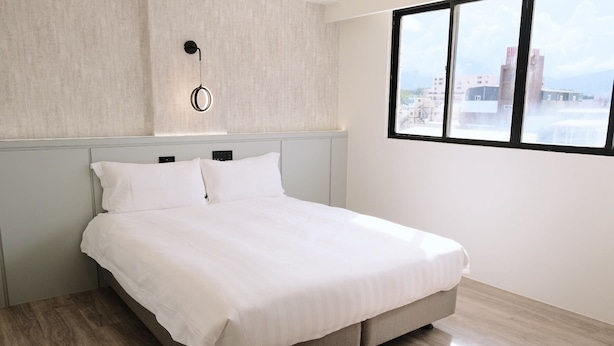 Een moderne slaapkamer met een bed, een wandlamp en een raam met uitzicht op de stad.