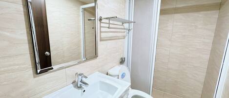 Et badeværelse med en hvid vask, et spejl, et toilet og en bruseniche.