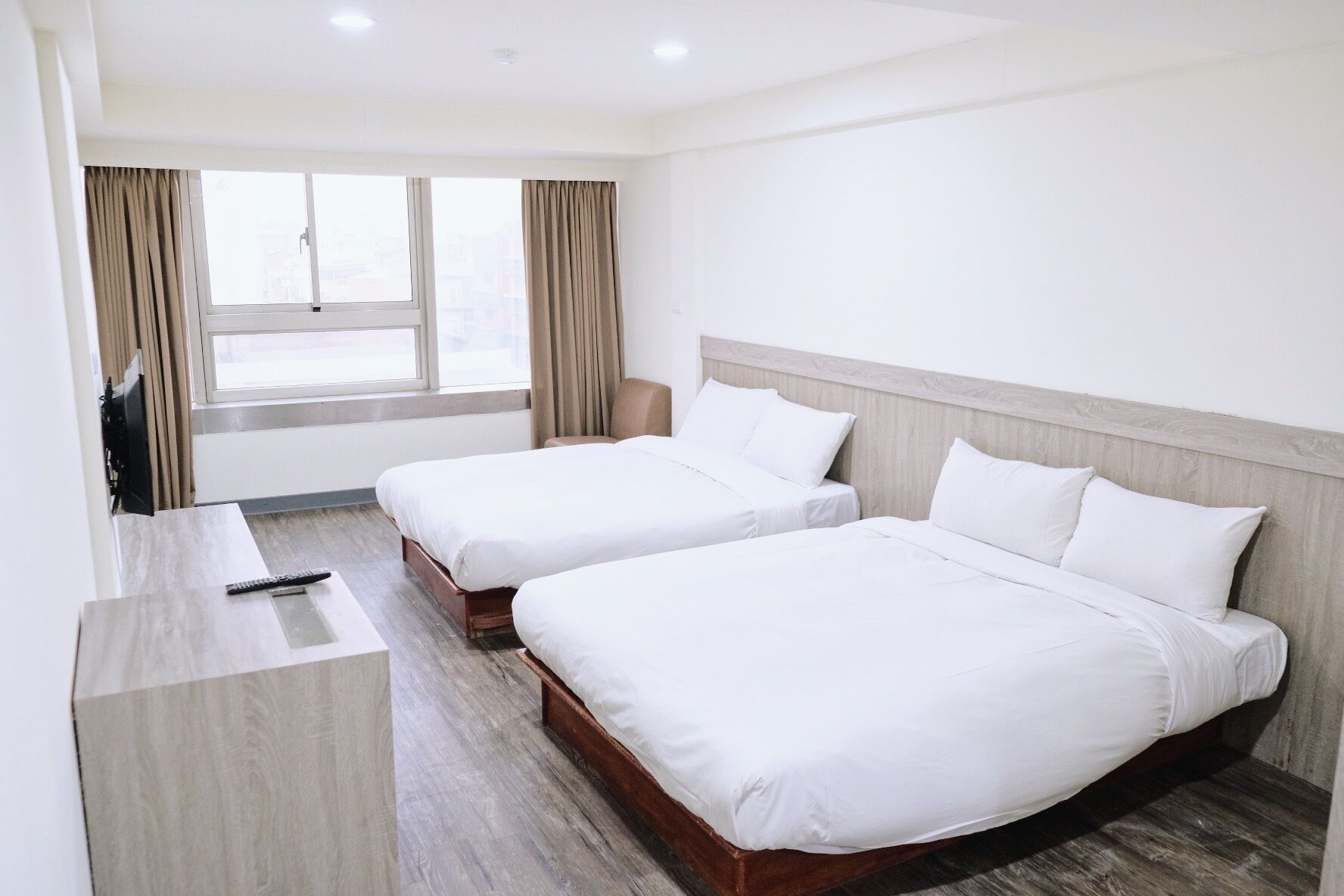 Quarto de hotel com duas camas de solteiro, uma escrivaninha com cadeira e janela com cortinas.