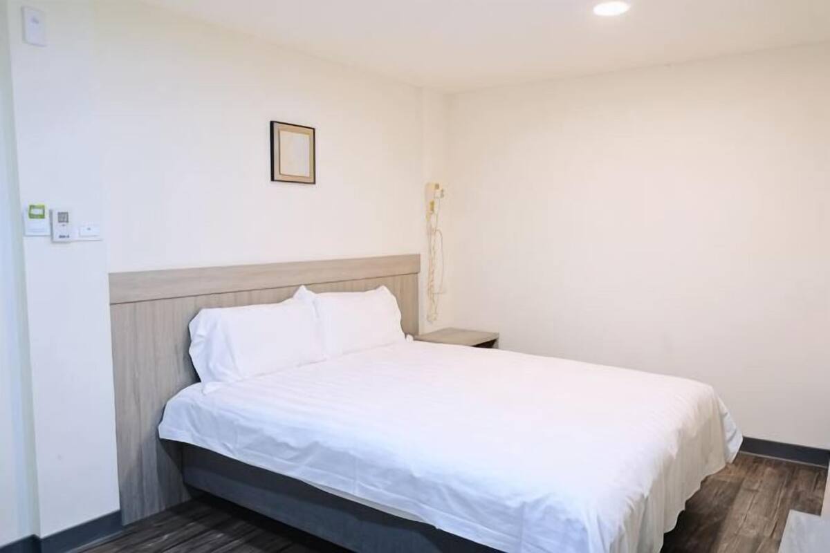 Una cama individual con cabecera de madera, una mesita de noche y una lámpara de pared.