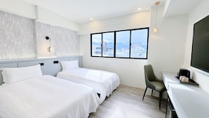Hotelkamer met twee bedden, een bureau, een stoel, een groot raam met uitzicht op de stad en een moderne lamp.