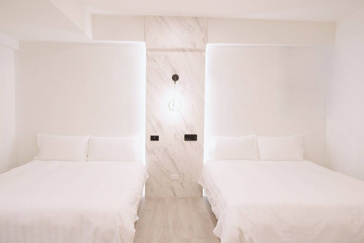 Habitación de hotel con dos camas individuales, una pared de mármol y una lámpara moderna.