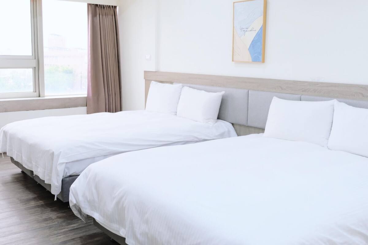Una habitación de hotel con dos camas individuales, un ventanal con cortinas y un cuadro en la pared.
