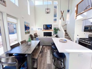 A modern kitchen with a large island, dining area with benches, and a fireplace. - Exceptional | New | Hot Tub & Pool | Sleeps 10! (Whitefish)