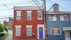 A two-story building with a red brick facade and a blue upper story. - Carey Way Quarters – Modern 2BR Near Carson Street (Pittsburgh)