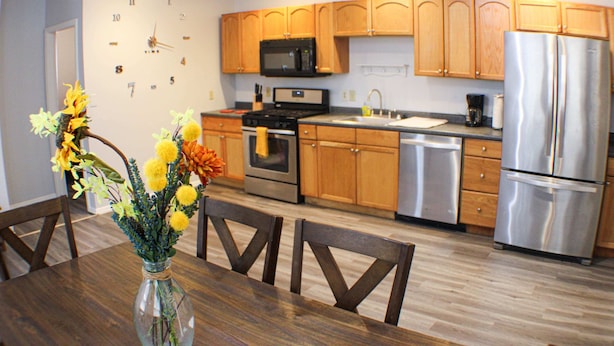 A modern kitchen with wooden cabinets, stainless steel appliances, and a dining area with a wooden table and chairs. - Carey Way Quarters – Modern 2BR Near Carson Street (Pittsburgh)
