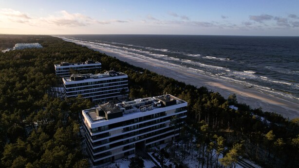 A modern building with multiple floors, surrounded by dense forest, overlooking a beach and ocean. - Campo Twoja Oaza w Shellter Rogowo (Trzebiatow)
