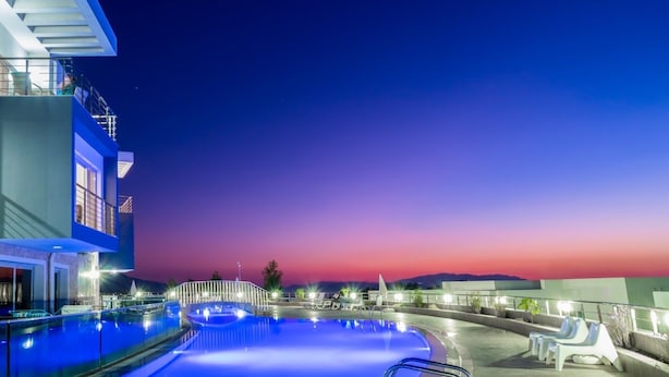 Ein Pool auf dem Dach mit freiem Blick auf den Sonnenuntergang, ein modernes Gebäude mit Balkon und ein gut beleuchteter Poolbereich.