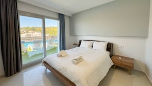 Et moderne hotelværelse med en stor seng, et trænatbord og udsigt til en swimmingpool gennem en skydedør.