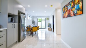 A modern kitchen with a dining area, a large window, and a colorful painting on the wall. - Royal Lake Guest House (Toukley)