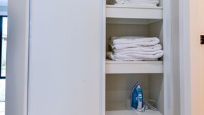 A white closet with shelves, one of which has folded towels and a blue cleaning bag. - Royal Lake Guest House (Toukley)
