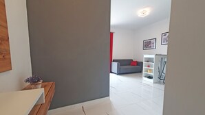 A modern living room with a grey sofa, a white coffee table, and a red cushion. There is a white bookshelf with various items and a framed picture on the wall. - Holiday Home Gordana - Charming Deluxe Apartment in fabulous Hvar (HVAR (HVAR))