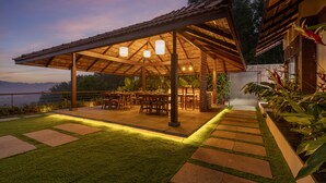 Un patio al aire libre con zona de estar techada, senderos de piedra y abundante vegetación.